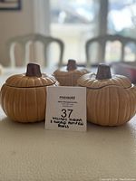 Three ceramic pumpkin bowls with lids shown from front, placed on a table with natural light from window background.
