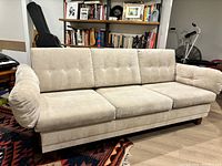 Front view of beige 3-seater sofa with button tufted back cushions, showing soft, plush cushions and rounded armrests in a living room setting.