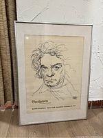 Framed print of Beethoven sketch with text, in a light-colored mat frame on a wall.