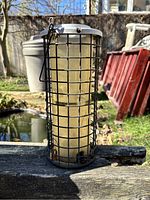 Outdoor photo of wire cage bird feeder on a wooden surface with garden background.