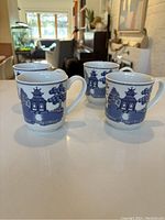 Set of four Blue Willow china mugs on a table with background furniture visible.