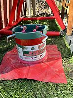 Metal Christmas tree stand with red and green colors sitting on a red cloth on grass.