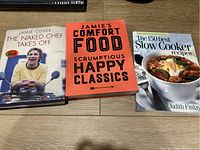 Three cookbooks laid flat on a wood surface: two by Jamie Oliver and one by Judith Finlayson.