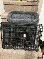 Black metal wire pet crate folded and grey plush dog bed on stair steps.