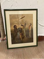 Framed print showing four children with a floating drumstick, green frame and white mat, leaning against a wall on wooden floor
