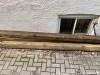 Two long wood planks laid on ground outside near a foundation window, showing weathering and natural discoloration.