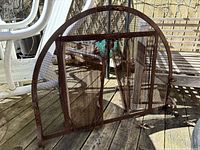 Rust-colored iron fireplace grate and semi-circular mesh fireplace screen shown outdoors on a wooden deck.
