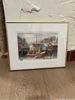 Framed watercolour painting showing a fishing harbour with boats and houses.