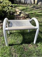 Photo of white outdoor footstool on grassy lawn with visible dirt and signs of weathering.