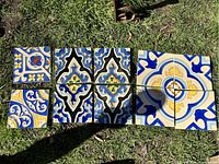 Ten decorative 6x6 glass tiles laid out on grass showing colorful patterns