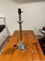 Silver lamp base standing on a wooden table, showing entire base and electrical cord with plug.