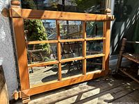 Mirror with large wood frame and grid dividing the reflective surface into nine sections, set outdoors on a deck with natural wood tone.