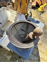 Top-down view of iron mortar showing conical mesh inside and wooden pestle.