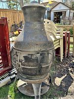 Front angle view of the rod iron fire pit showing mesh cage and chimney with weathered, rusted surface.