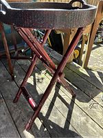Close-up side angle showing the cherry-coloured wood frame with foldable legs and the rattan tray top with built-in handles.