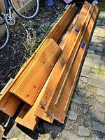 Photo of wooden shelving boards stacked outside, showing varying lengths with metal rail system for adjustable brackets.