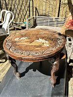 Full view of round rosewood side table showing carved elephant figures on legs and inlay top surface with some damage.