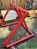 Red PVC tubular skating helper support frame on outdoor stone floor, showing angled joints and rubber caps on tube ends