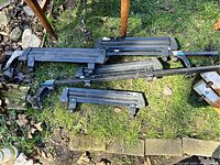 Photo showing multiple black metal and plastic parts of a car ski rack laid on grass, including crossbars and mounting attachments.