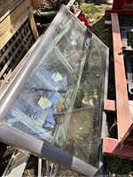 Skylight window laid on side outside, showing its rectangular glass and metal frame structure with some surroundings reflected in the glass.
