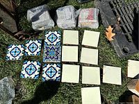Multiple ceramic tiles laid out on grass, showing both plain off-white and blue patterned tiles in groups.
