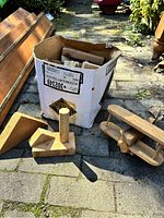 Photo of cardboard box on outdoor pavement with numerous wooden blocks around it and a wooden biplane toy beside it.