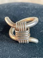 Close-up front view of the sterling silver knot ring showing the wrapped parallel bands and curved bars on a dark fabric background.