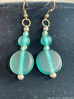 Front view of pair of green frosted glass earrings showing round disc bead at bottom and smaller round beads above
