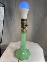 Full view of the lamp lit with a blue glowing LED bulb to show working condition, revealing the jadeite glass base and antique metal socket.