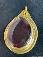 Front view of vintage pendant showing purple glass cabochon and gold-tone metal setting.