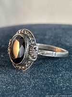 Close-up side angle of vintage sterling silver ring featuring an oval faceted black onyx center stone surrounded by marcasite stones, showing band detail and condition.