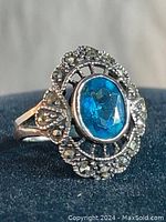 Front angled view of vintage sterling silver ring with bright blue aquamarine center stone and marcasite accents around.