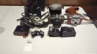 Overview of lot including Canon and Pentax cameras, Fujifilm digital camera, binoculars, opera glasses, flash unit, and cases