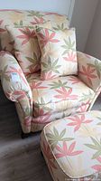 Full view of the upholstered chair with two cushions and matching ottoman showing floral pattern and rolled arms.