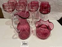 Group view showing eight cranberry stem glasses arranged in back with cranberry pitcher and vase in front, all featuring diamond and star cut pattern