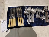 Full set of mismatched EP cutlery laid out on a cloth including knives, forks, spoons, and ladles.