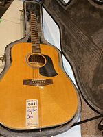 Full view of acoustic guitar in open hardshell case showing natural wood finish and black pickguard