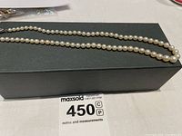 Pearl necklace displayed on a black box showing the entire strand laid out, highlighting the size gradient of the pearls and overall length.