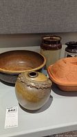 Large pottery bowl with brown speckled glaze, decorative pottery vase with rustic rim, glazed storage jug, and terracotta baking mold on table