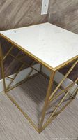 Square side table with white marble top and gold metal frame, showing top surface and metal base design.