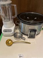 Overview photo showing slow cooker, blender, brass ladle, and two small metal measuring cups on white surface