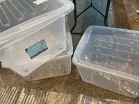 Three clear resin storage bins stacked and placed on floor, showing lids, casters, and transparent sides.