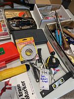 Overview photo showing assortment of tools and hardware including vintage Dremel Moto-Tool in box, screwdrivers, hammer, measuring tape, foam mounting strips, and other items.