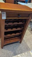 Front view of wooden wine cabinet showing drawer with black knob and four bottle racks inside