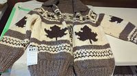 Front view of chunky knit wool jacket showing brown and cream color scheme with maple leaf pattern and zipper closure.