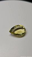 Photo of a pear-shaped lemon citrine gemstone displaying a deep bright yellow color with detailed facets on a plain background.