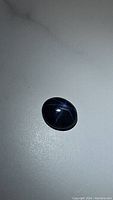 Loose oval cabochon sapphire viewed under flash, showing 6-ray star across surface