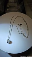 Photo showing the pendant necklace laid flat, displaying the round moissanite gemstone set in silver and adjustable chain length with clasp.