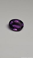 Close-up photo of a deep purple oval cut Brazilian amethyst gemstone showing high luster and faceting details.