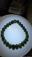 Photo of a round bead green jade bracelet on a stretchy cord, showing rich green polished beads arranged in an oval shape.